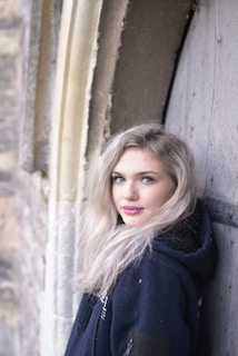 woman in black coat standing beside brown wooden wall