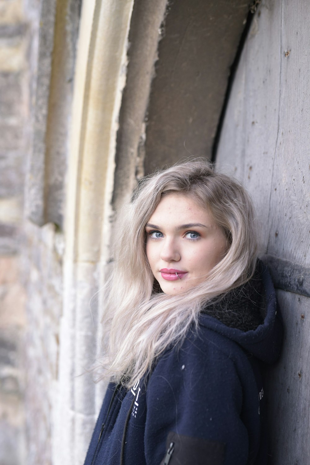 woman in black coat standing beside brown wooden wall