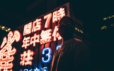 Anime character with glowing eyes standing under neon signs at night.