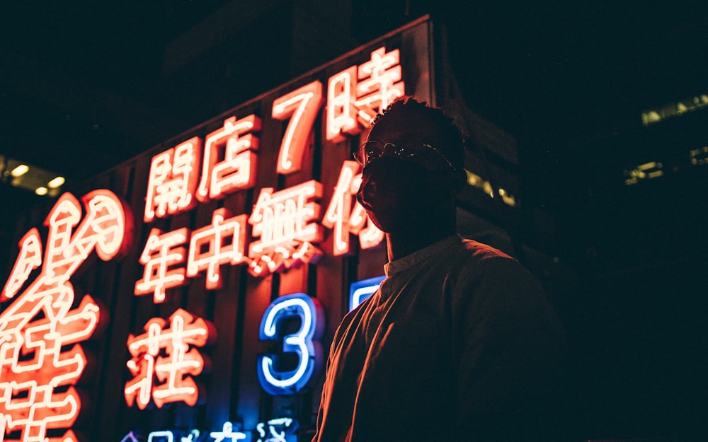 man in black hoodie standing in front of red and white led signage