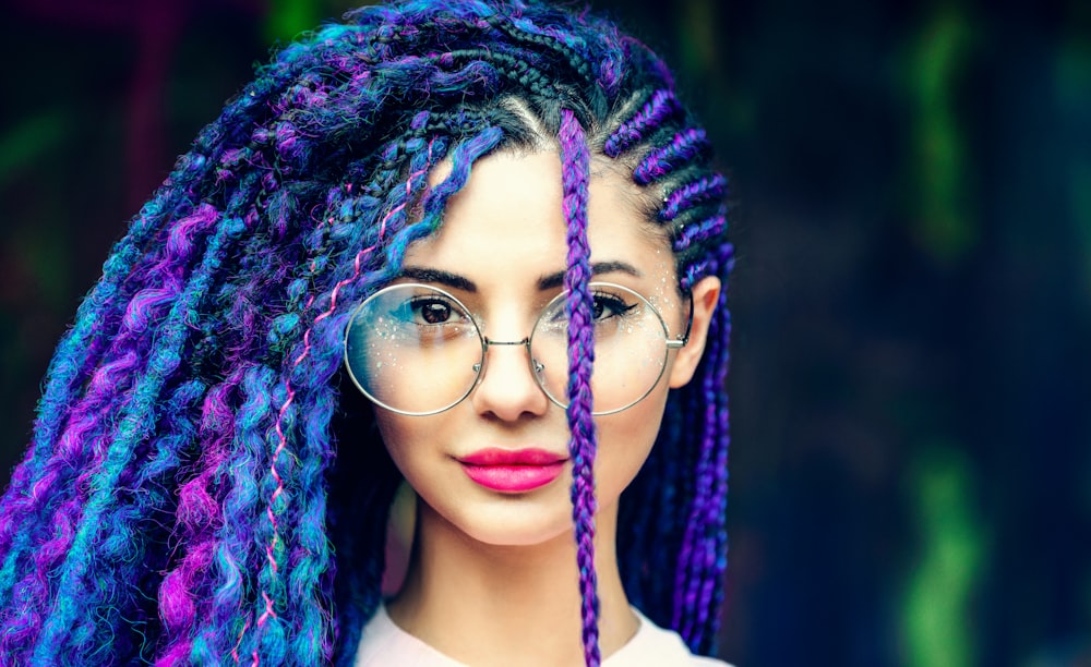 mujer con cabello azul con camiseta sin mangas blanca y anteojos con montura azul