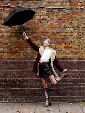 woman in black skirt holding umbrella standing beside brick wall