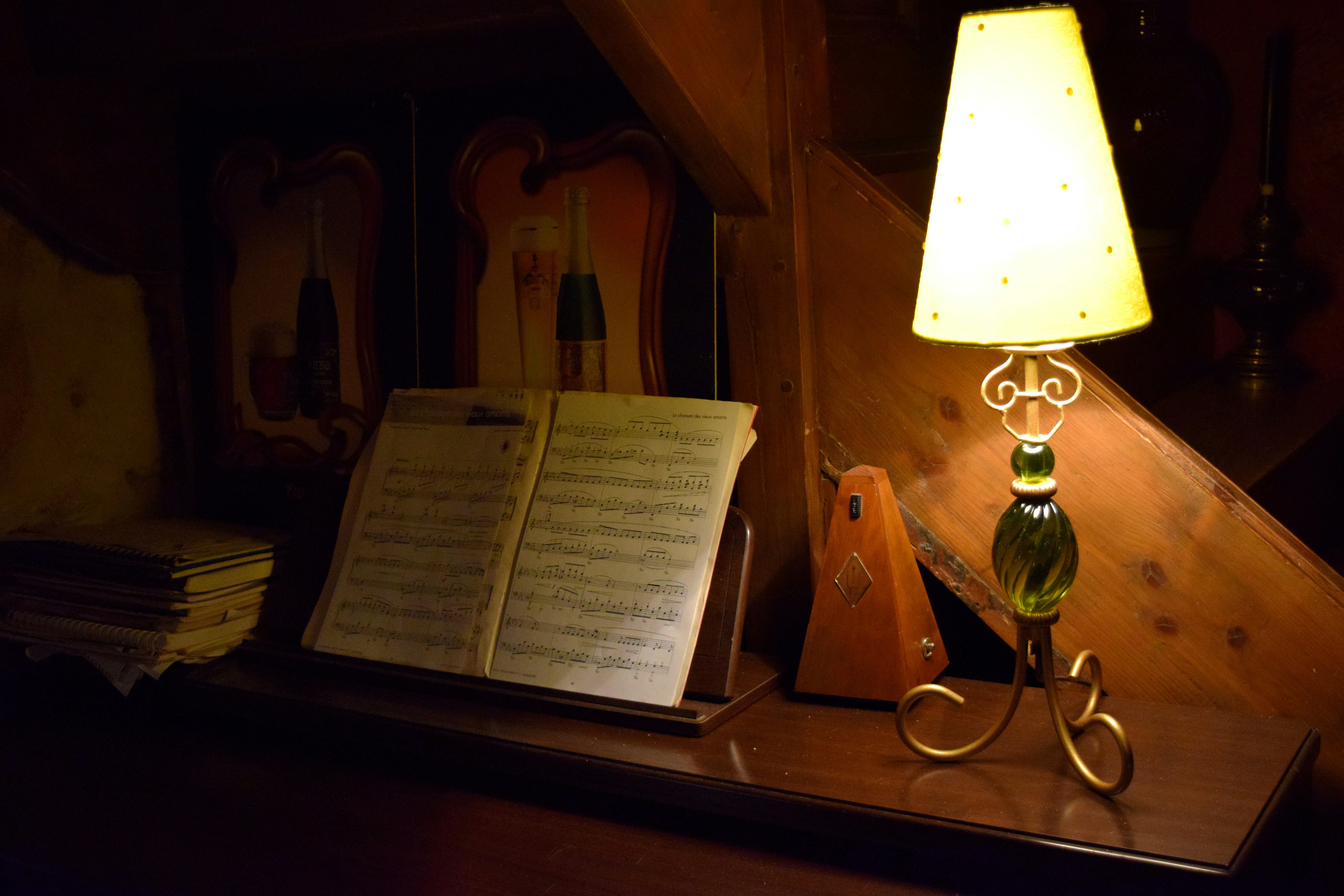 A lamp-lit spinnet-style piano with a metronome off to the side