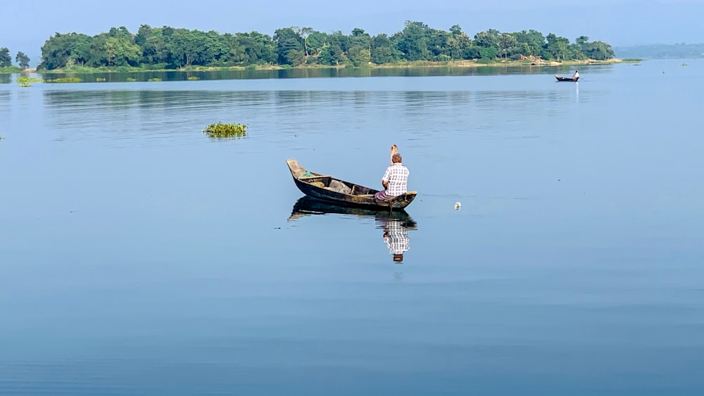 白いシャツと茶色の短パンを着た男性が、昼間、水域で茶色のボートに乗っている
