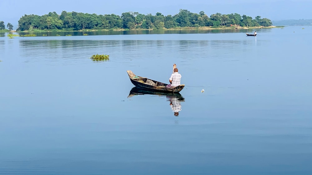 man in white shirt and brown shorts riding brown boat on body of water during daytime