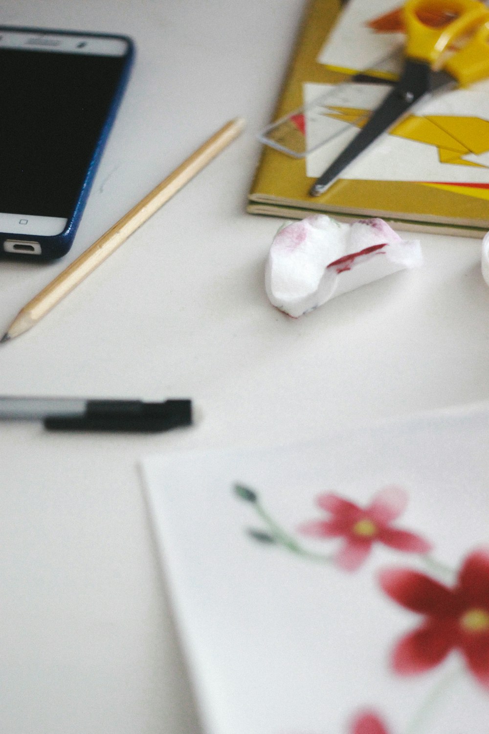 schwarzer Klickstift neben weißer und roter Blume auf weißem Tisch