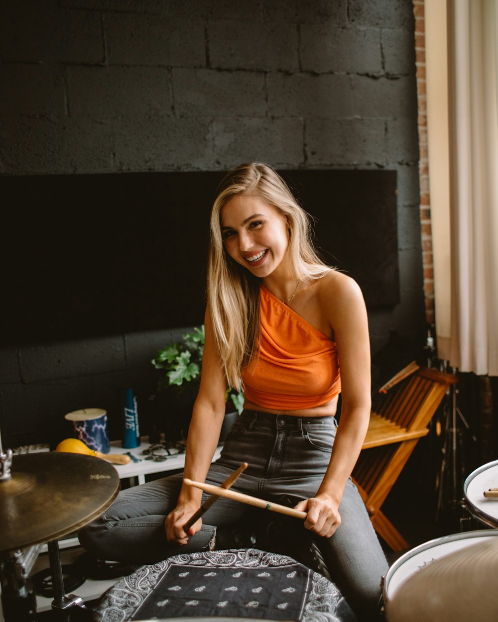 woman in orange tank top holding brown wooden drum stick