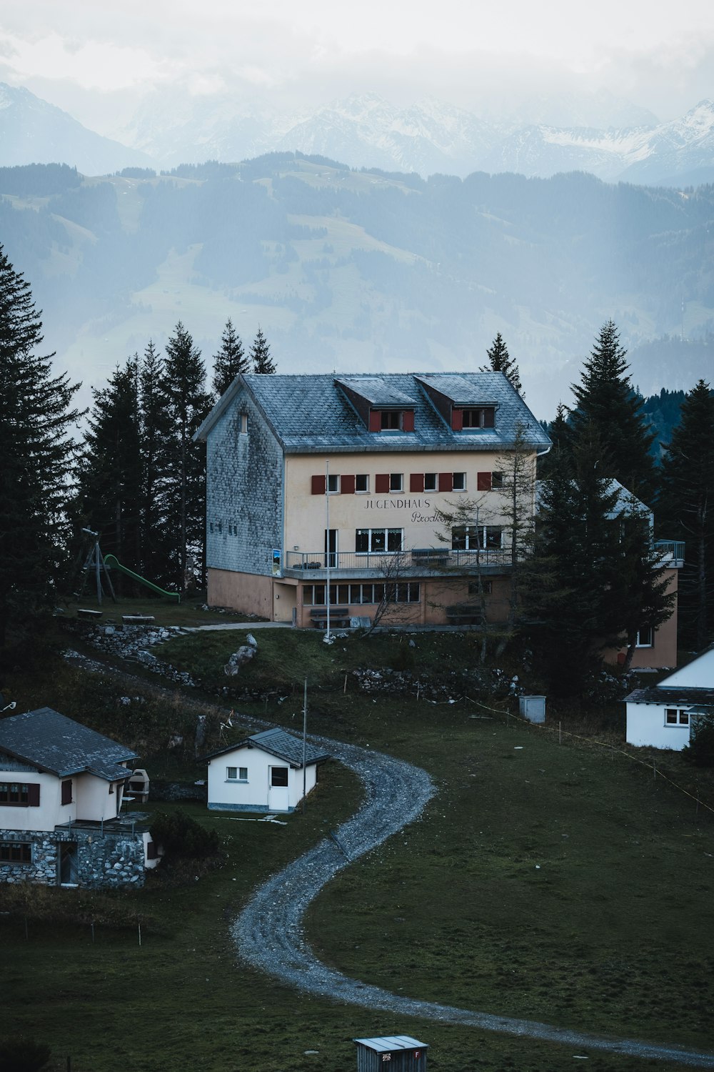 white and brown concrete house near green pine trees under white clouds and blue sky during