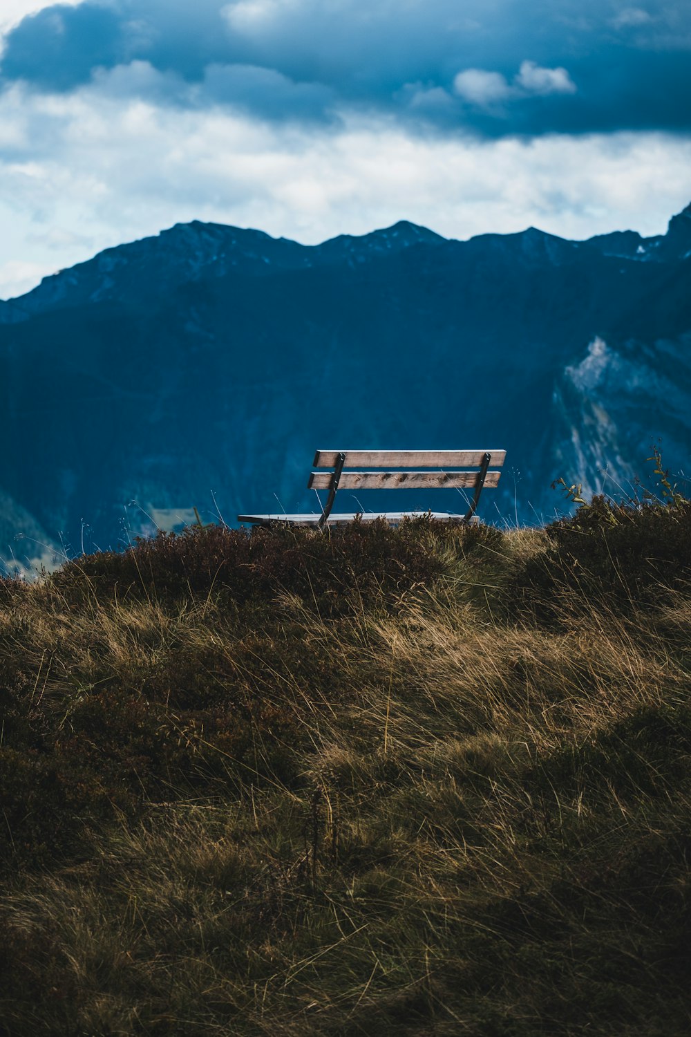 brown wooden bench on green grass field near mountain during daytime