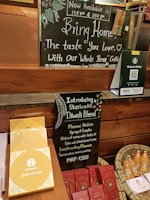 A display at Starbucks promoting a Diwali blend coffee. The setup includes a chalkboard with handwritten details, including flavor notes and pricing for the new blend. A basket with bottled juices and boxes of chocolates are also featured. A QR code stand is present for ordering options.