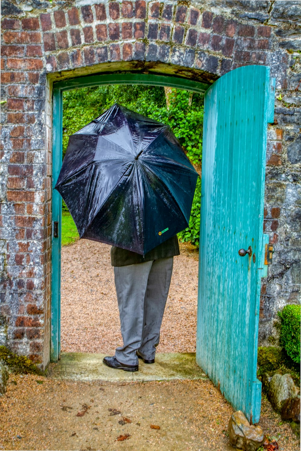 Person in schwarzem Regenschirm steht neben blauer Holztür