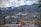 A large, historic hotel sits amidst a snowy forest with majestic mountains in the background. The wooden fence in the foreground adds a rustic touch to the scene. The sky is partly cloudy, and the setting conveys a sense of tranquility and grandeur.