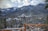 A large, historic hotel sits amidst a snowy forest with majestic mountains in the background. The wooden fence in the foreground adds a rustic touch to the scene. The sky is partly cloudy, and the setting conveys a sense of tranquility and grandeur.