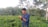 A farmer inspecting fresh spices in a lush green field under a clear blue sky.