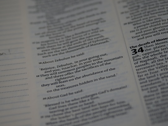 The image features a close-up view of a page from a book, likely a Bible, with text that includes chapters and verses. The sections are organized with headings in bold, and the text is printed in black on white paper.