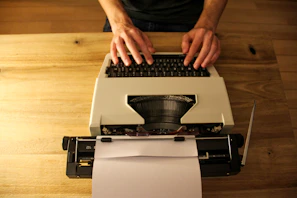 A close-up of hands typing on a vintage typewriter with scattered papers around.