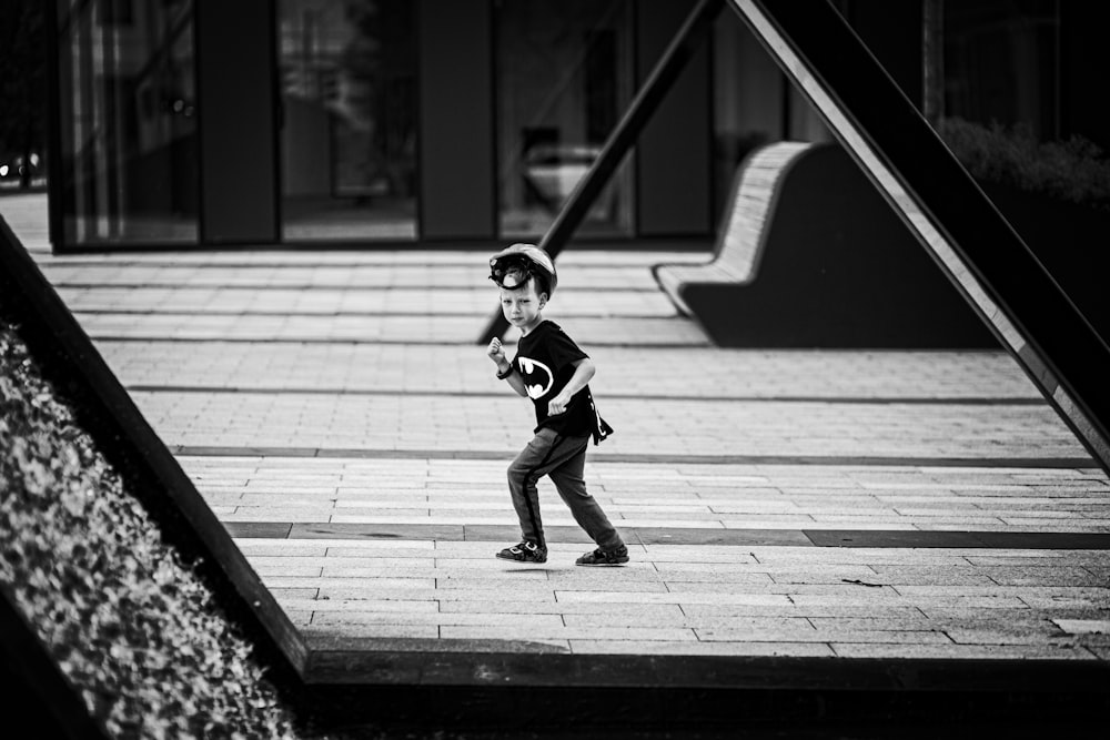 grayscale photo of boy in black shirt and pants running on sidewalk