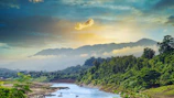 A serene aerial shot capturing a sunset over a winding river in lush green mountains.
