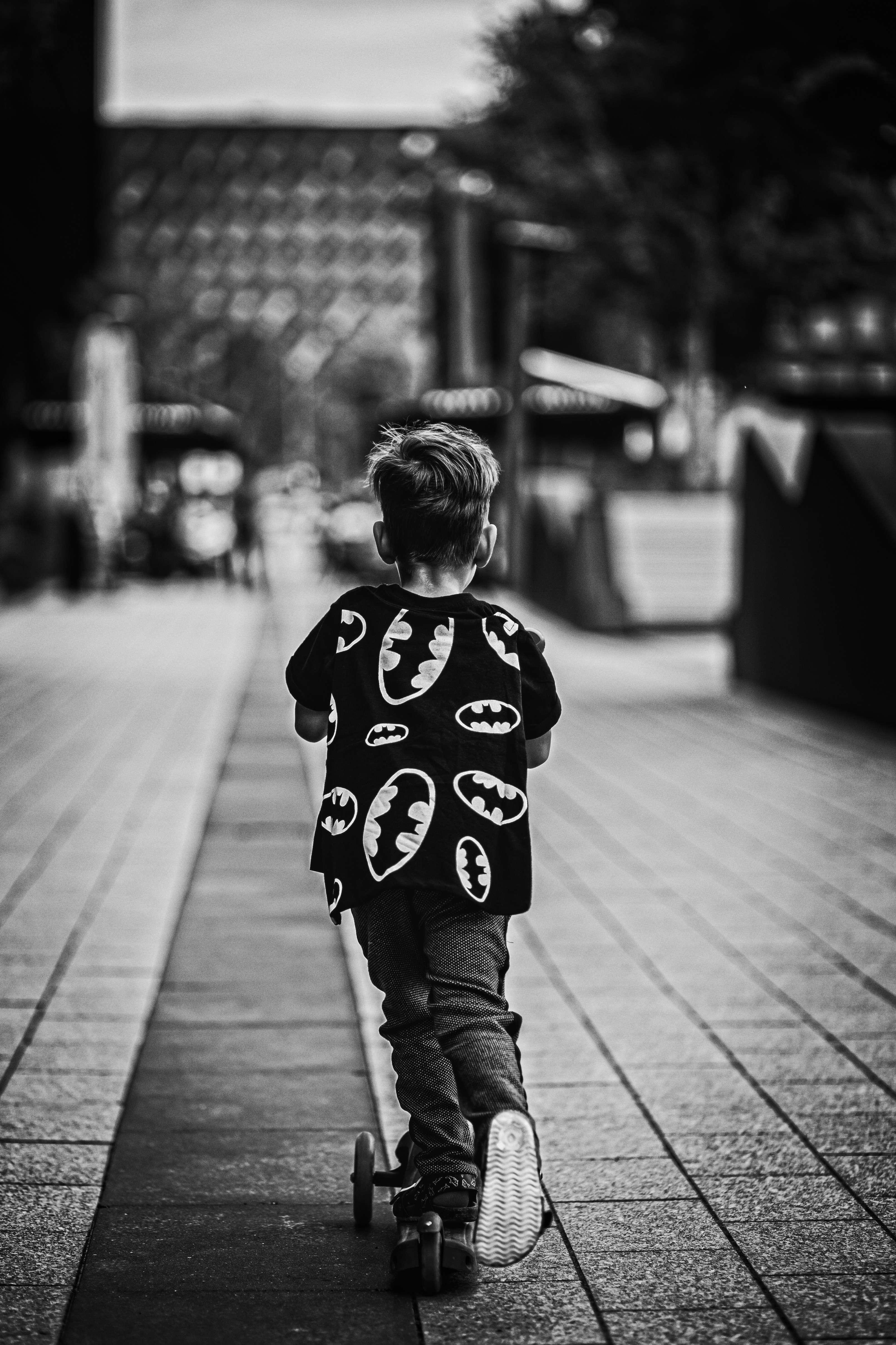 grayscale photo of child in mickey mouse shirt and pants walking on sidewalk