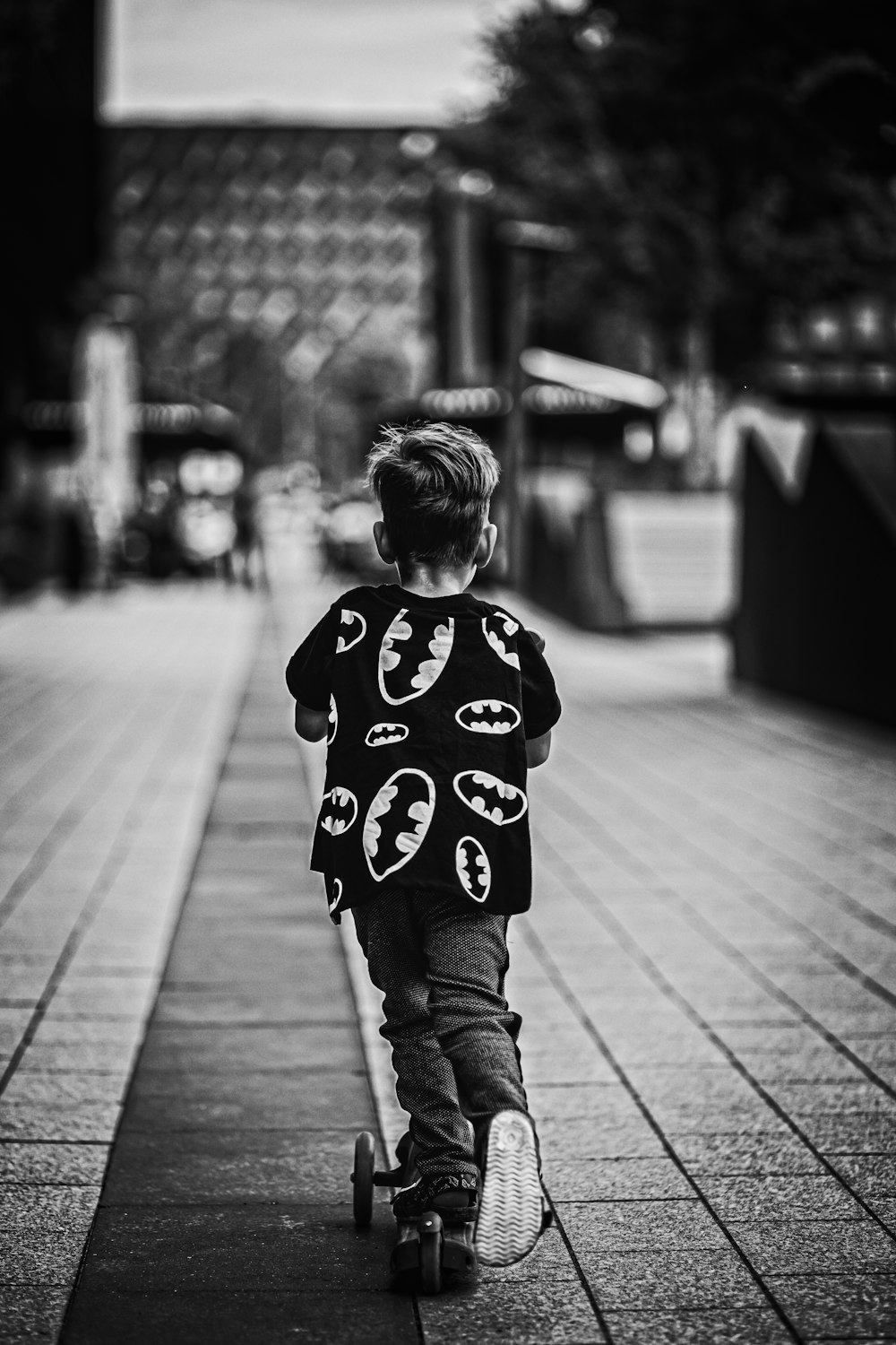 grayscale photo of child in mickey mouse shirt and pants walking on sidewalk