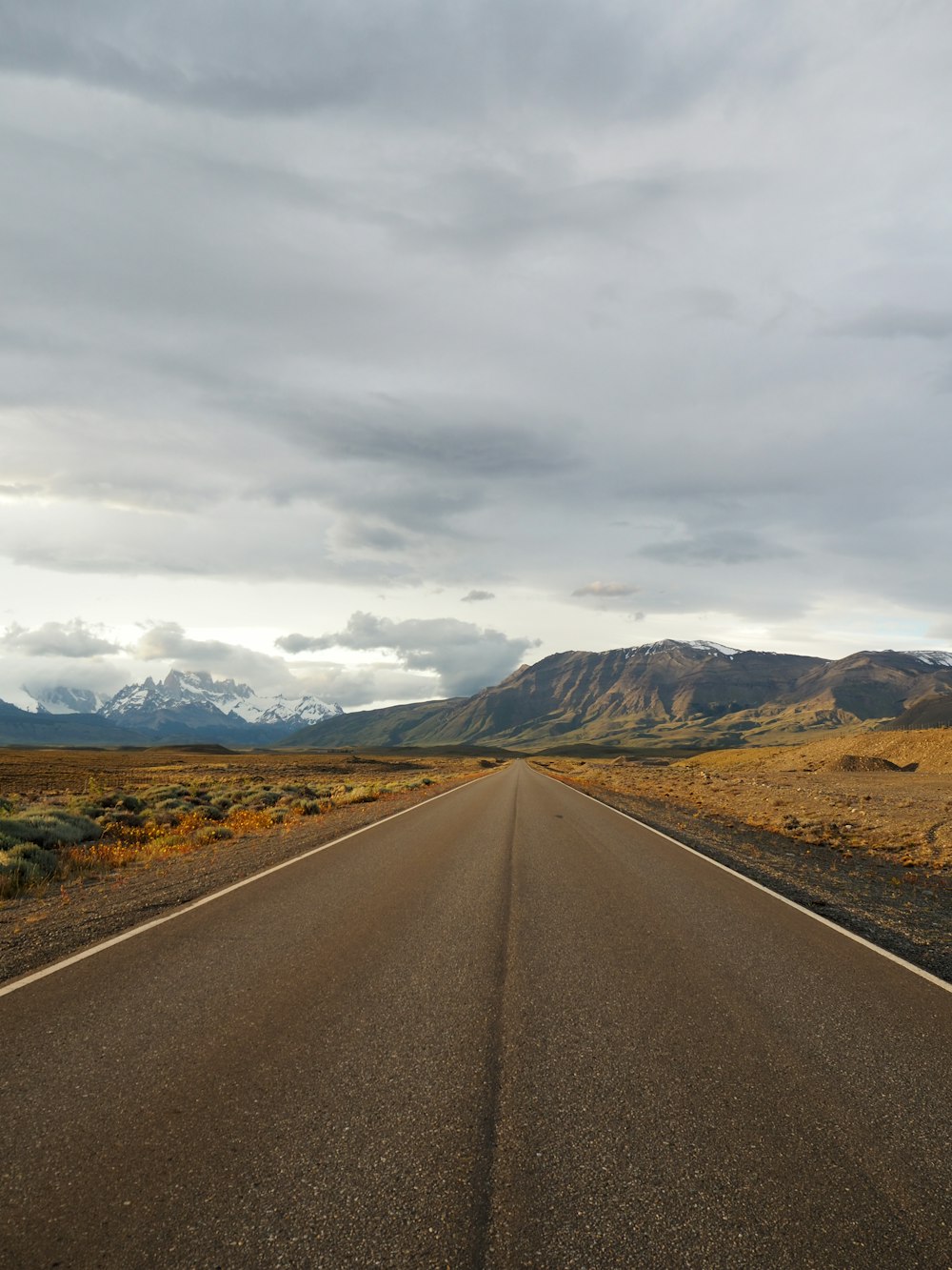 gray asphalt road between brown grass field under white cloudy sky during daytime