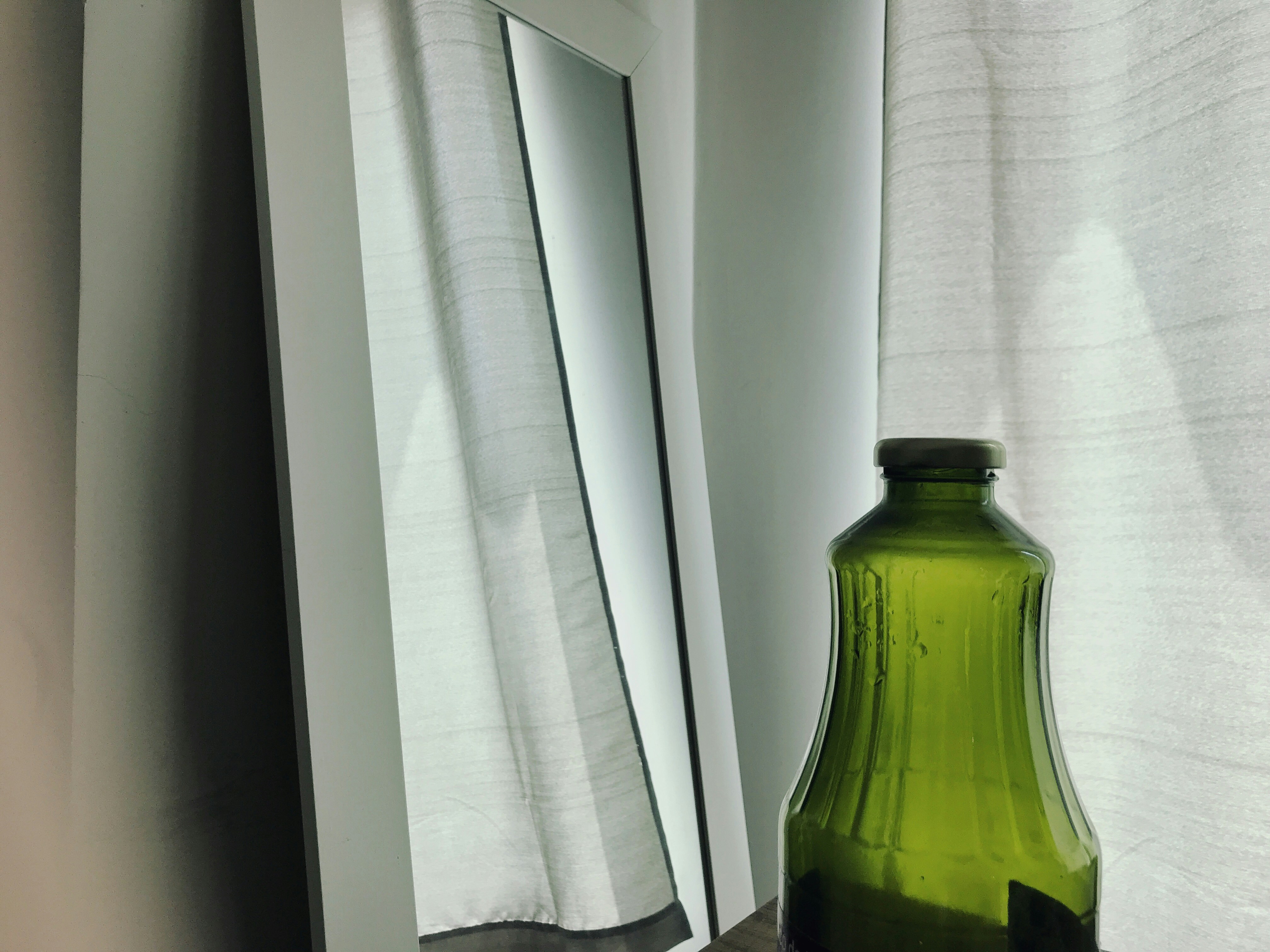 A mirror by the window with a bottle in the front<br />