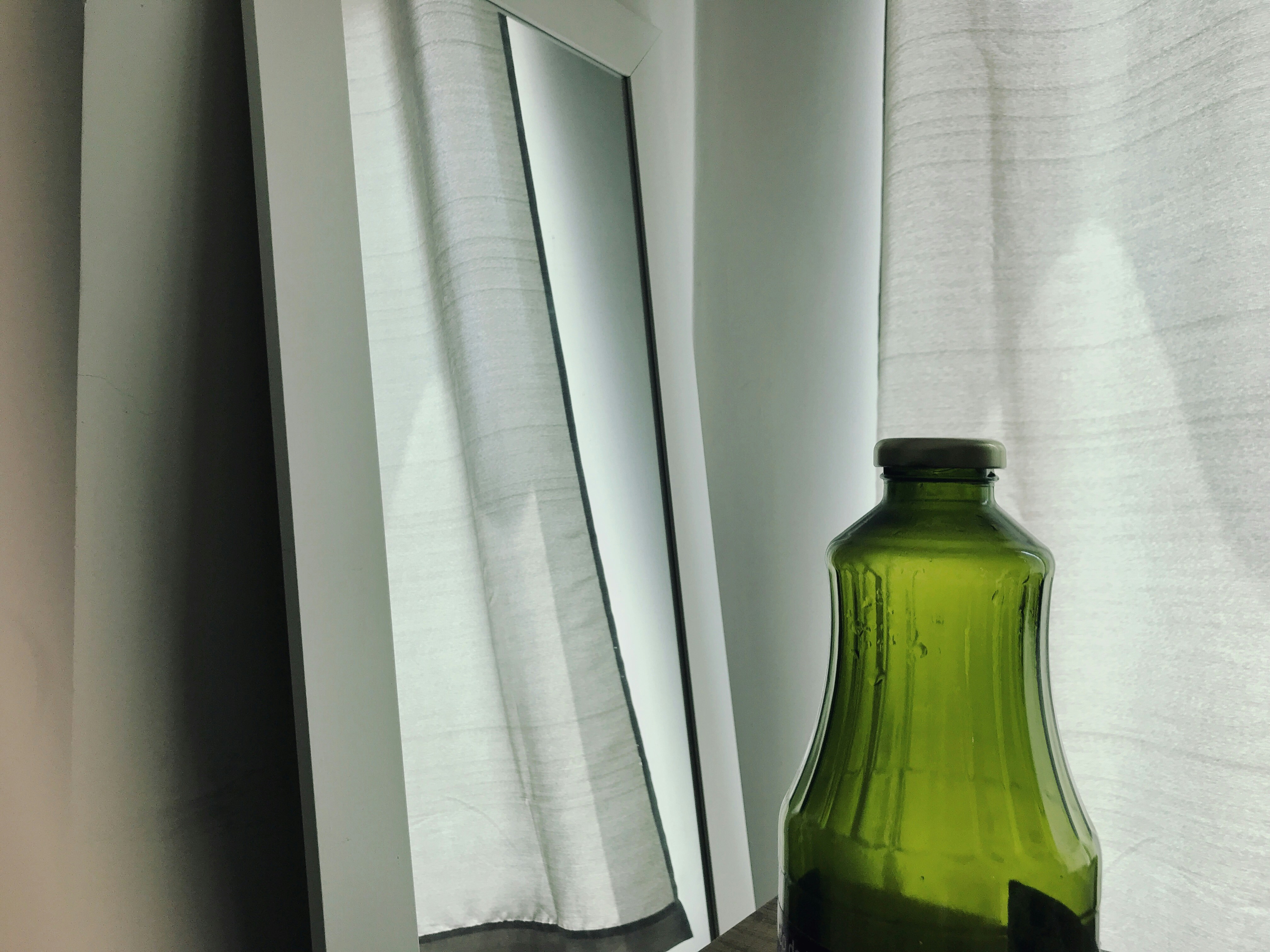 A mirror by the window with a bottle in the front