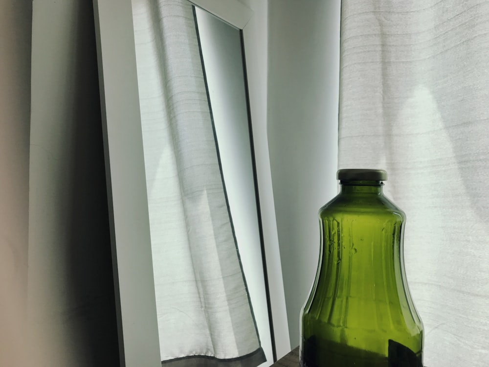 green glass bottle near white window curtain