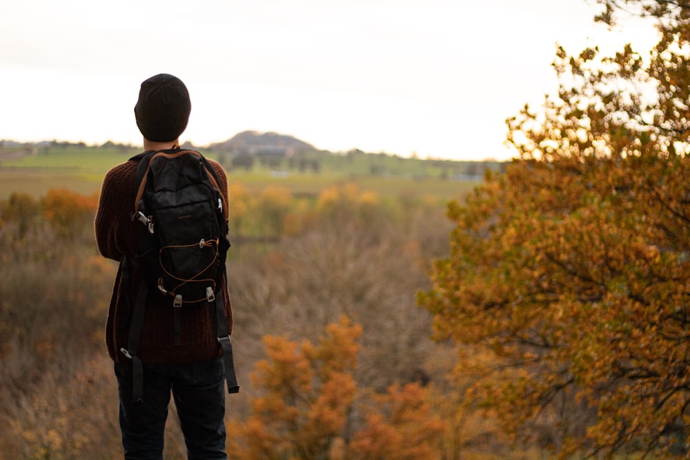 man in black jacket and blue denim jeans standing in front of brown trees during daytime