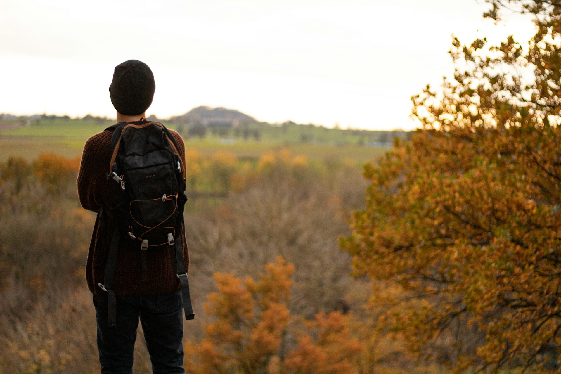 man in black jacket and blue denim jeans standing in front of brown trees during daytime