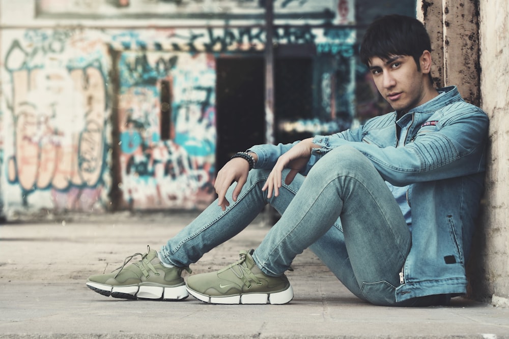 man in blue denim jacket and blue denim jeans sitting on floor