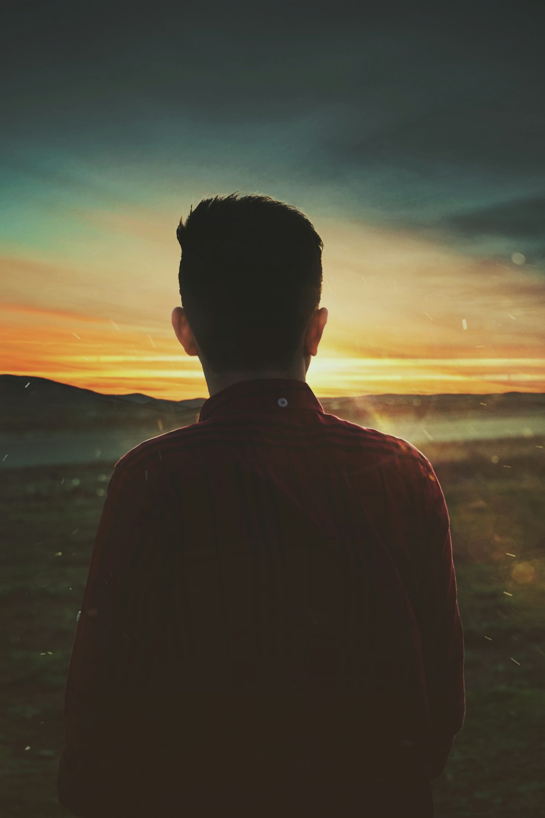 man in black jacket standing near body of water during sunset