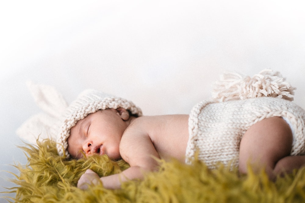 Baby in weißer Strickmütze auf grünem Textil liegend