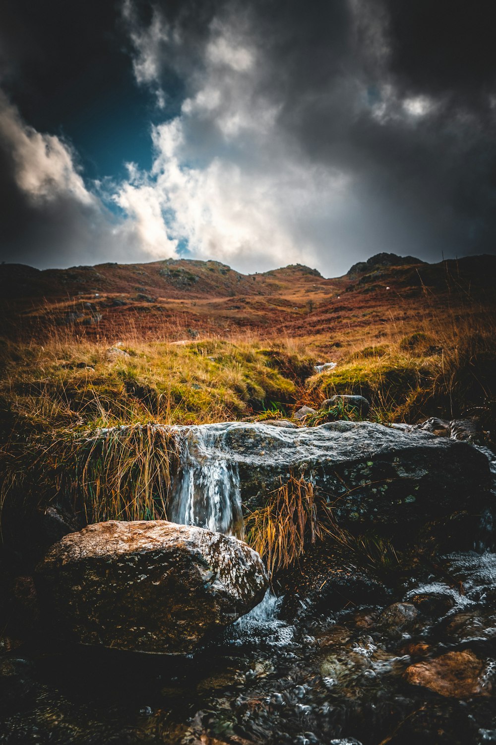 water falls on brown mountain under gray clouds