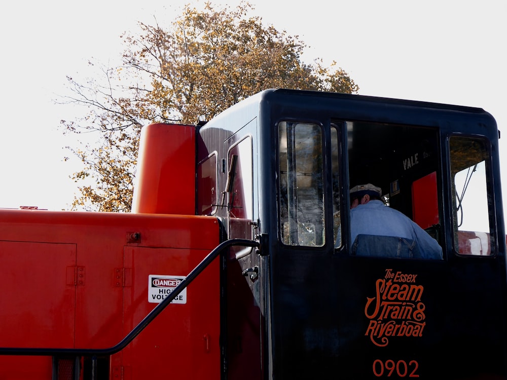 man in black jacket standing beside red and black truck during daytime