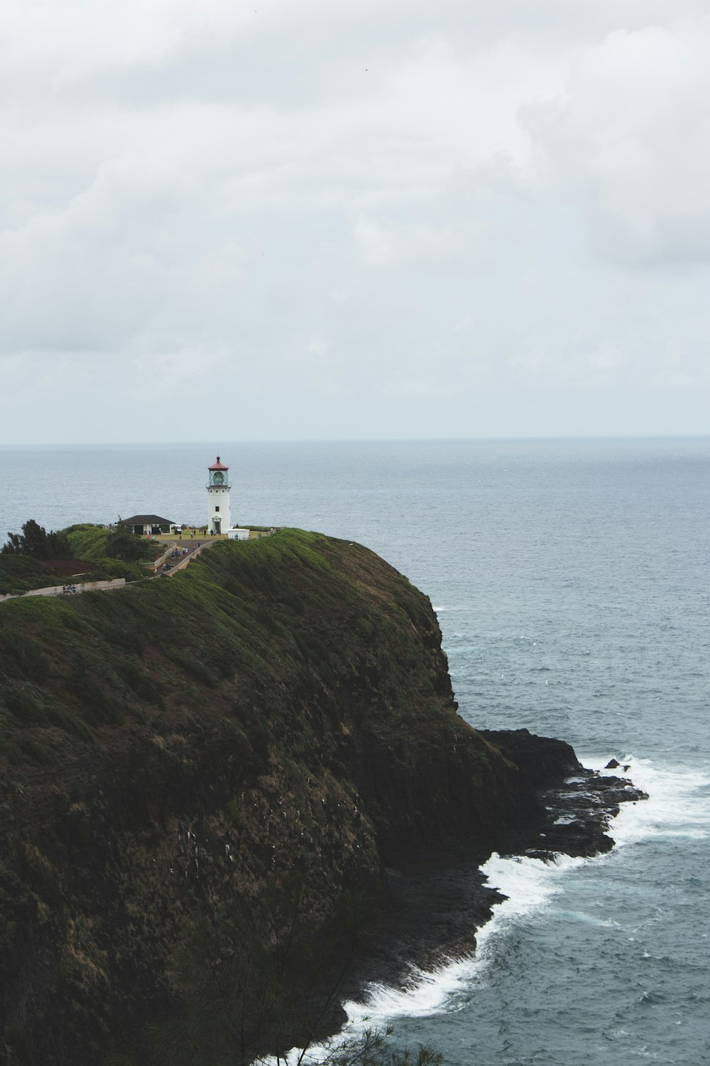 white and red lighthouse on top of mountain near body of water during daytime