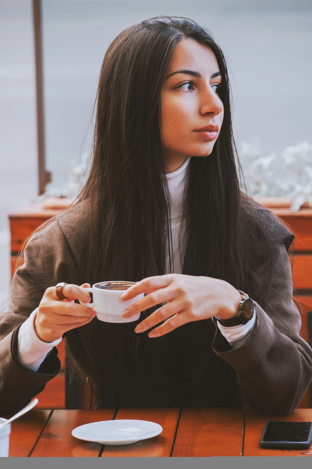woman in brown coat holding white ceramic mug