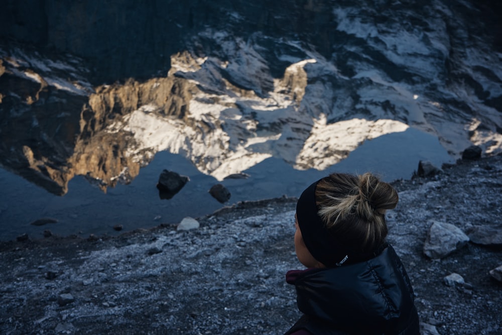 person in black jacket sitting on gray rock near snow covered mountain during daytime