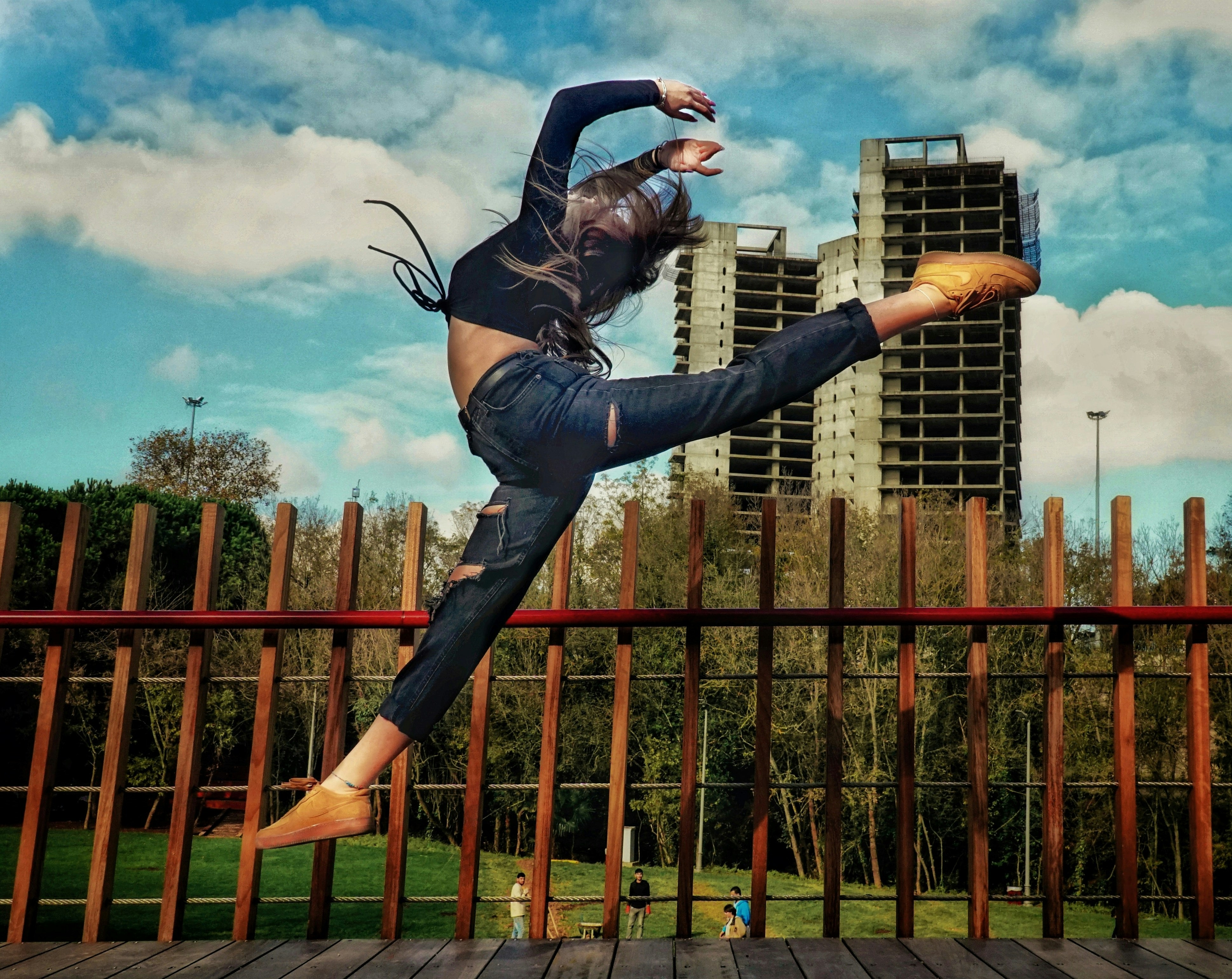 woman in black jacket and blue denim jeans jumping on brown wooden fence during daytime