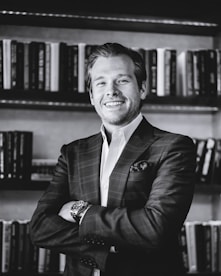 Black and white photo of a male author smiling warmly with bookshelves behind.