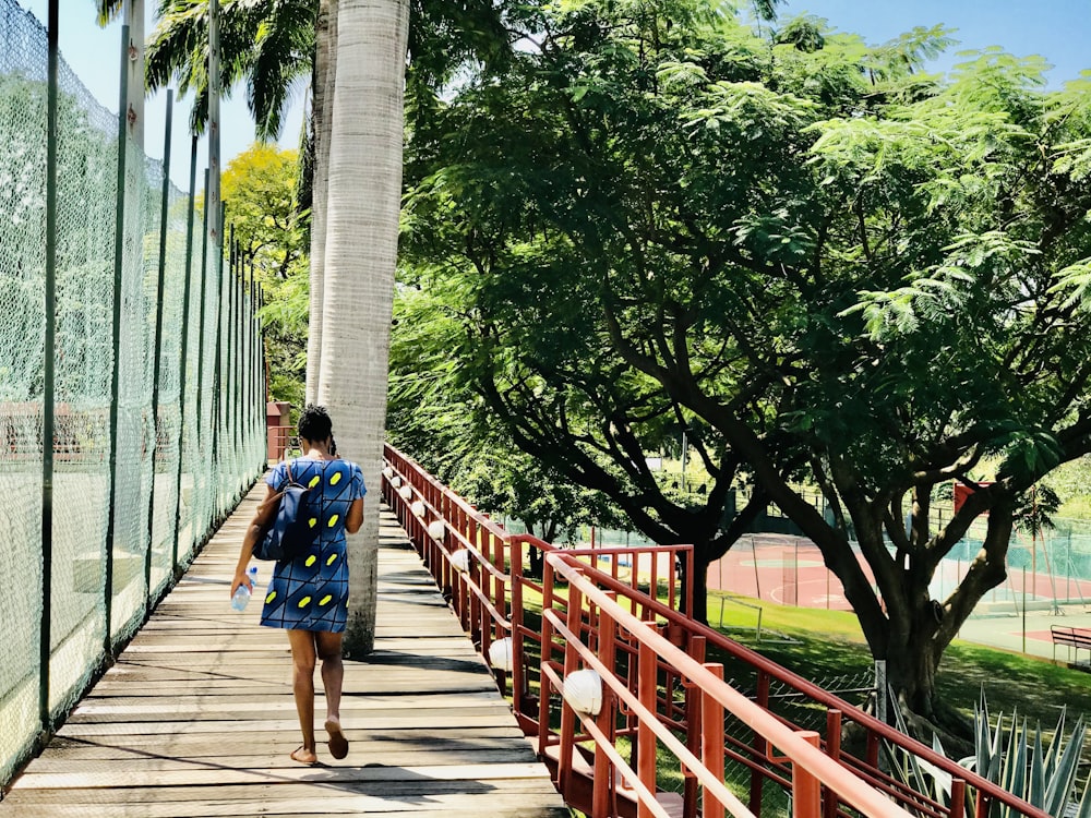 uomo in zaino blu e nero che cammina sul ponte di legno durante il giorno