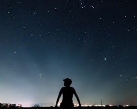 A person gazing thoughtfully at a glowing horoscope wheel under a starry night.