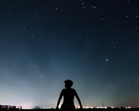 A silhouette of a person watching meteors with binoculars under a clear starry sky
