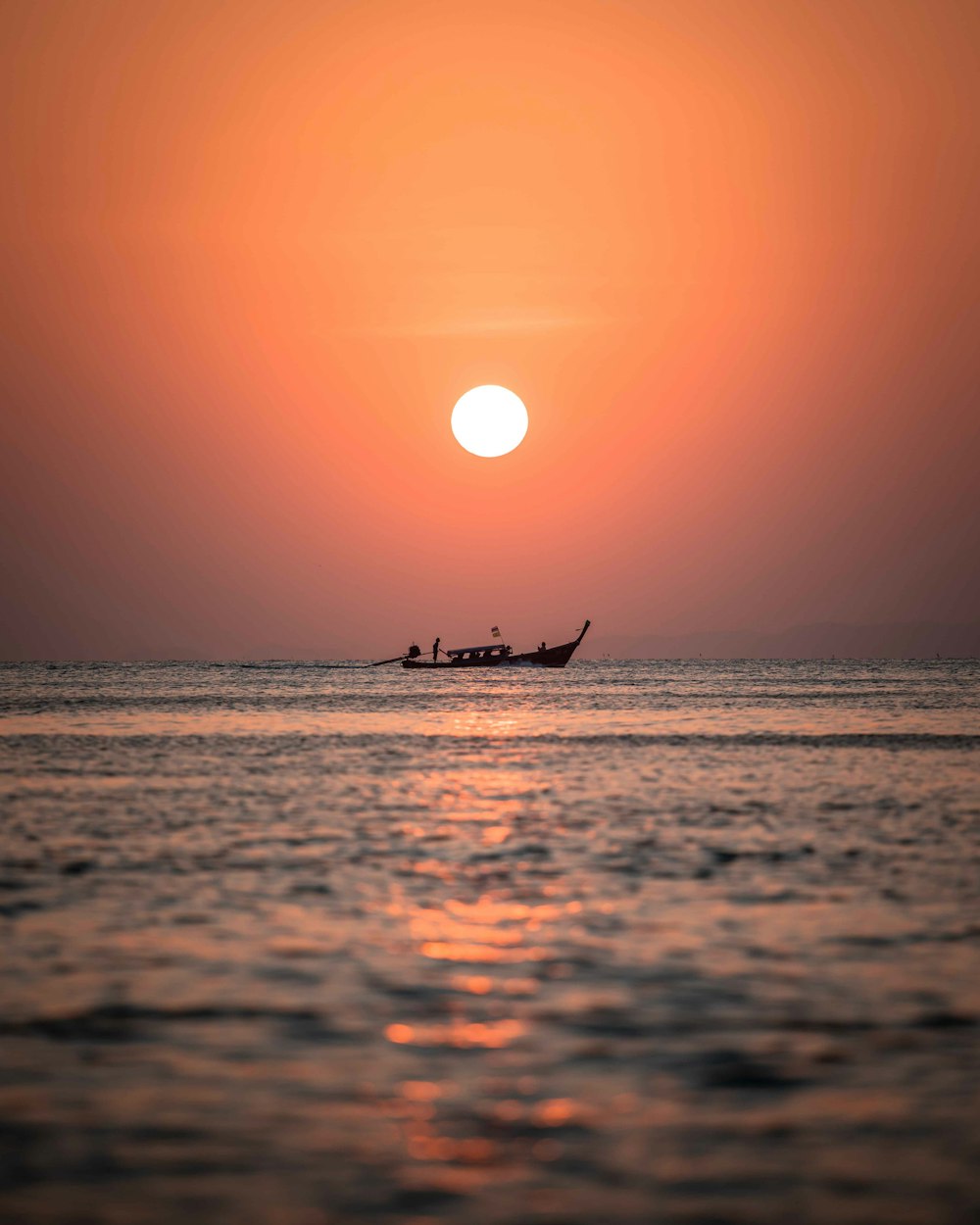 a boat in the ocean with the sun setting in the background