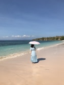 woman in white dress holding pink umbrella walking on beach during daytime