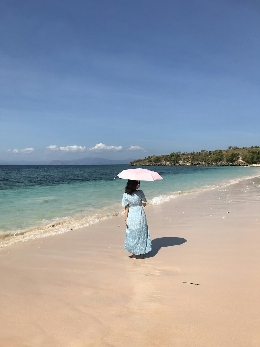 昼間にビーチを歩くピンクの傘を持つ白いドレスの女性