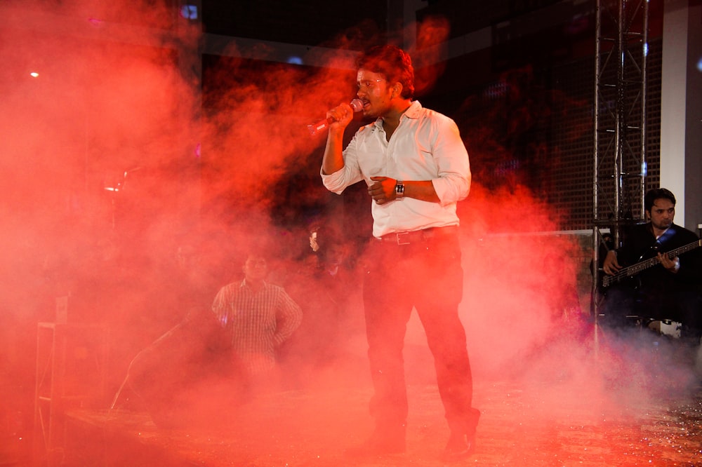 homem na camisa social branca e calças marrons cantando no palco