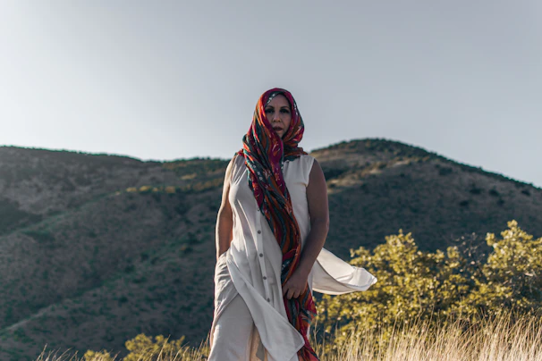 Close-up of a hijab fabric with breathable, sweat-wicking texture in terracotta color, held against a backdrop of mountain peaks.