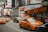 A busy urban street scene featuring yellow taxis driving alongside a double-decker bus with 'Big Bus New York' signage. Surrounding buildings are adorned with large advertisements and electronic billboards, typical of a bustling city atmosphere.
