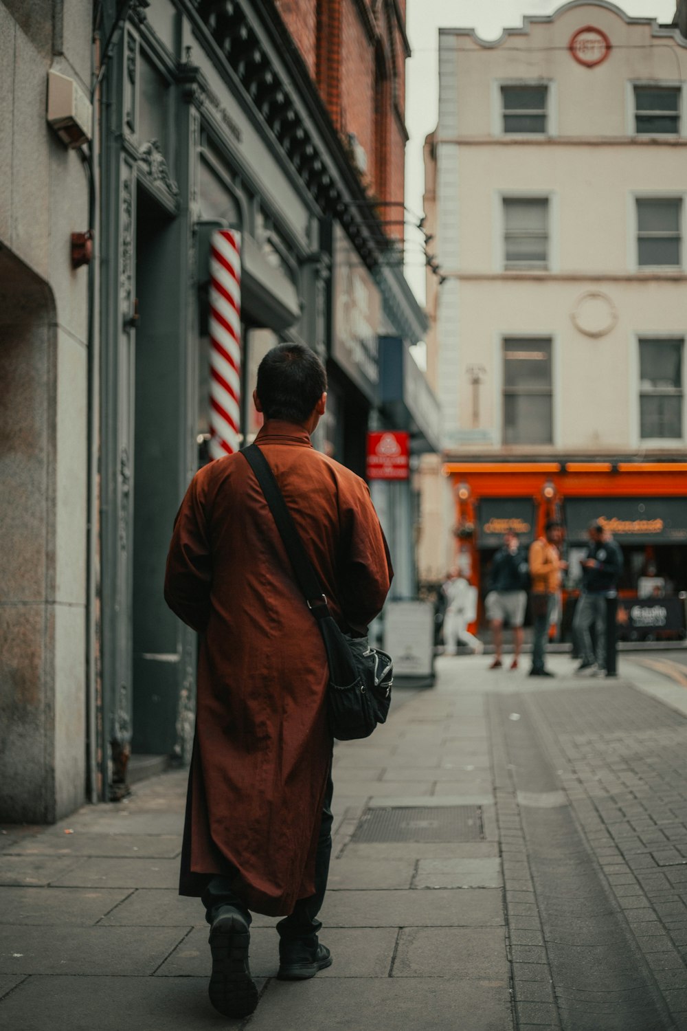 man in red coat walking on sidewalk during daytime